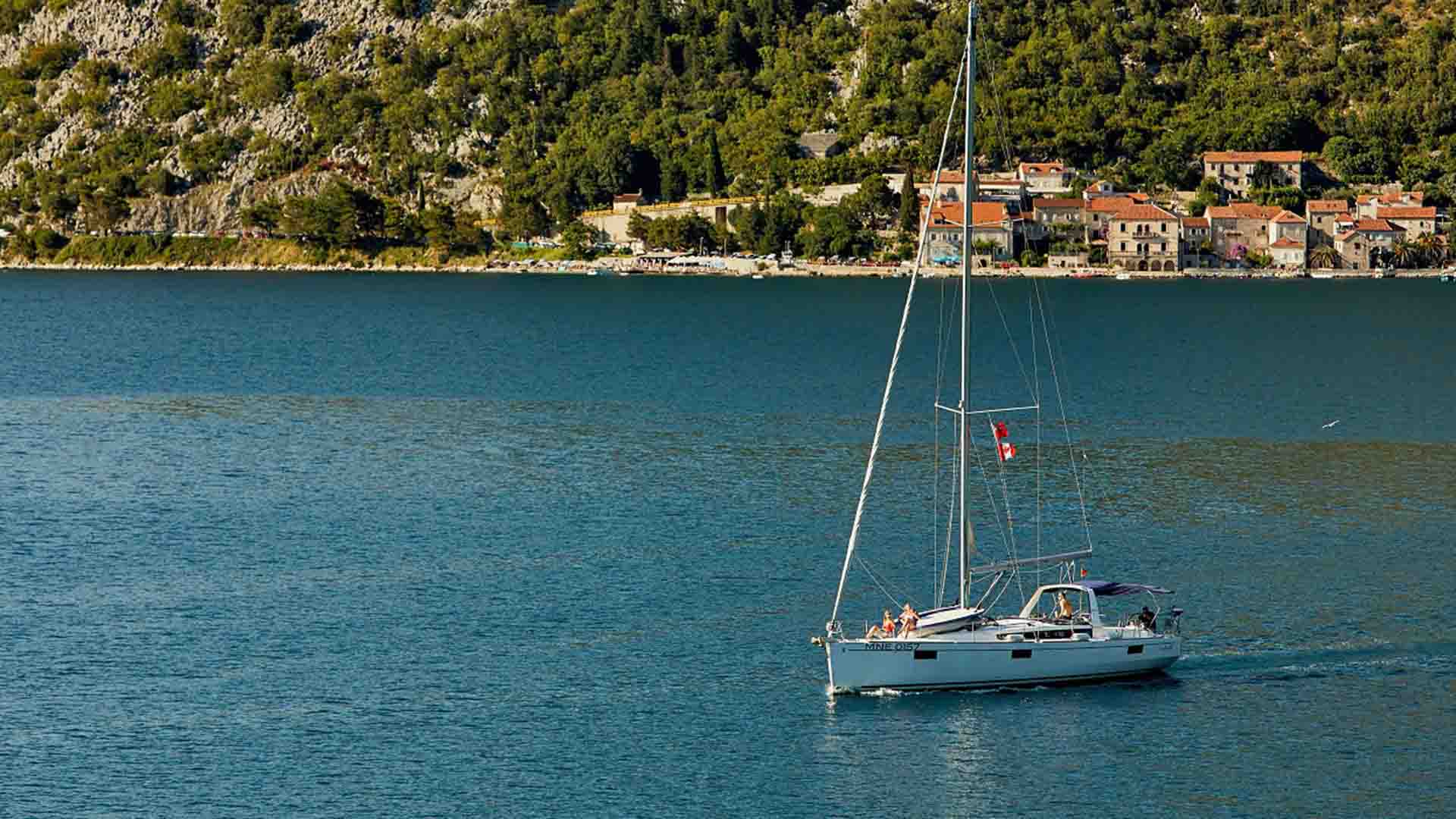 Yacht sailing in Boka bay, Kotor, Montenegro, with small town of Perast behind.